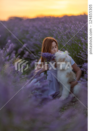 A woman sits in a field of purple flowers with a dog A woman sits in a field of purple flowers with a dog 124855305