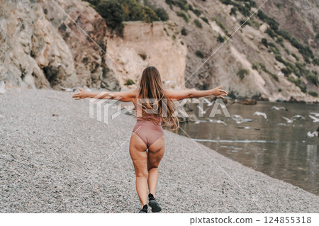 A woman with long hair is walking on a beach. She is wearing a bikini and she is enjoying herself. 124855318