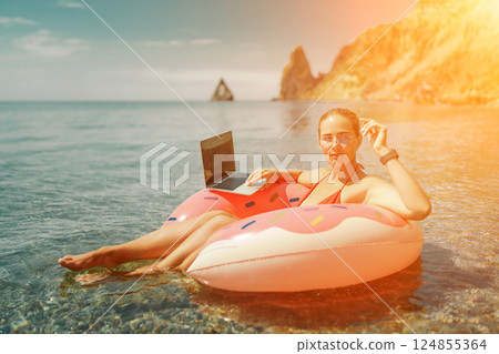 Woman laptop sea. Freelancer woman in sunglases floating on an inflatable big pink donut with a laptop in the sea. People summer vacation rest lifestyle concept 124855364