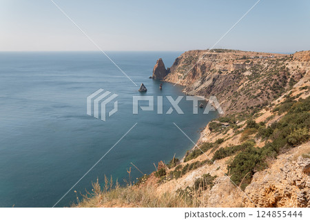 A beautiful ocean view with a rocky shoreline. The water is calm and the sky is clear. A beautiful ocean view with a rocky shoreline. The water is calm and the sky is clear. 124855444