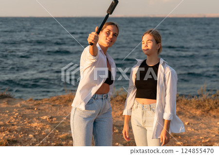 Selfie, Beach, Women: Two women take a selfie with a selfie stick while standing on a beach at sunset. Selfie, Beach, Women: Two women take a selfie with a selfie stick while standing on a beach at sunset. 124855470