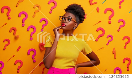 Young pensive african american woman in casual clothes and eyeglasses touching chin and looking away thoughtfully while making decision against yellow wall with many colorful question marks and arrows 124855625
