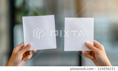 Woman's hands holding two blank white square papers, symbolizing the dilemma of choosing between options and the anxiety of decision making 124856231