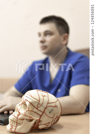 model of a human skull with blood vessels, in the background a doctor man is a blurred silhouette 124856891