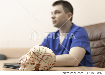 model of a human skull, in the background a doctor man is a blurred silhouette model of a human skull, in the background a doctor man is a blurred silhouette 124856892