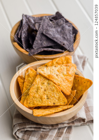 Dark and yellow nachos chips in bowl on white table. 124857039