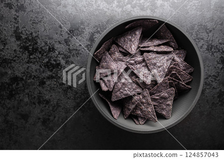 Dark nachos chips in bowl on black table. Top view. Dark nachos chips in bowl on black table. Top view. 124857043