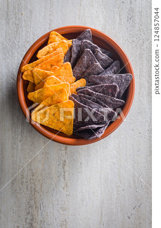 Dark and yellow nachos chips in bowl on kitchen table. Top view. 124857044