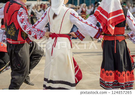 People dressed with traditional Bulgarian authentic folklore clothes dance Bulgarian dance. Close-up of dancers in folk costumes holding hands back view. Traditional dance People dressed with traditional Bulgarian authentic folklore clothes dance Bulgarian dance. Close-up of dancers in folk costumes holding hands back view. Traditional dance 124857265