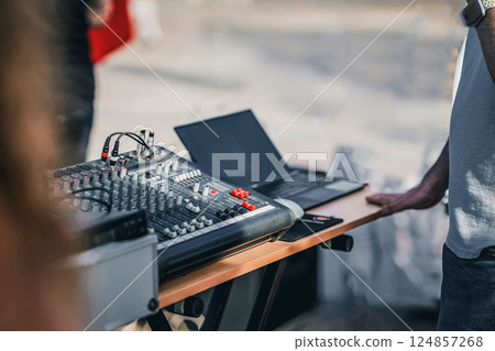 Professional audio mixing console with laptop set, outdoor event. Sound engineer adjusting settings for live performance, high-quality audio output. Sound mixer for music control, performance setup 124857268