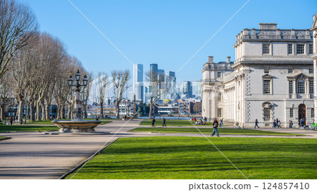 Visitors stroll through the beautifully landscaped grounds of the Old Royal Naval College in Greenwich. The stunning architecture contrasts with the modern skyline in the background. 124857410