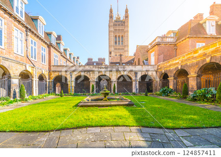 Visitors enjoy the serene green lawn of the Cloisters at Westminster Abbey in London. The historic architecture surrounds the lush space, creating a peaceful atmosphere for reflection. 124857411