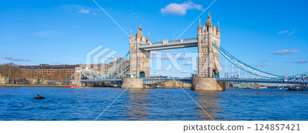Tower Bridge stands majestically over the River Thames, showcasing its stunning architecture against a clear blue sky. Visitors enjoy the vibrant atmosphere along the waterfront. 124857421