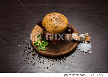 A pot with baked meat and a bread lid on a wooden A pot with baked meat and a bread lid on a wooden 124857723
