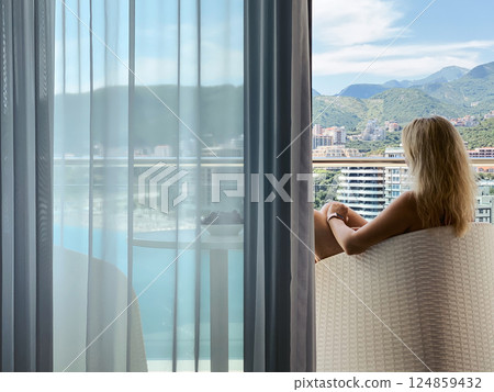 A woman sits on a balcony enjoying the view of the sea and mountains 124859432