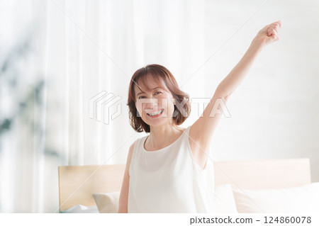 Middle-aged woman doing fist pump in bed in the morning Middle-aged woman doing fist pump in bed in the morning 124860078