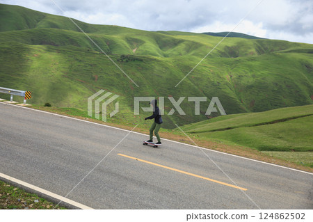 Skateboarder skateboarding on the mountain road Skateboarder skateboarding on the mountain road 124862502