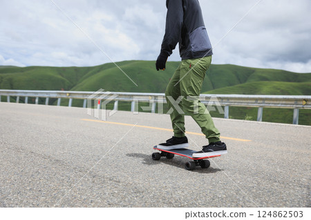 Skateboarder skateboarding on the mountain road Skateboarder skateboarding on the mountain road 124862503