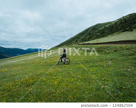 Aerial view of woman riding mountain bike on flowering grassland mountain 124862504