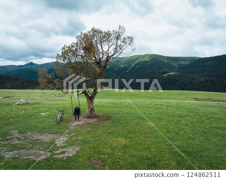 Aerial view of woman riding mountain bike on flowering grassland mountain 124862511