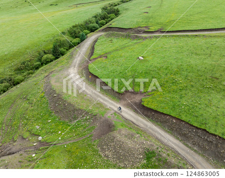 Aerial view of woman riding mountain bike on flowering grassland mountain trail Aerial view of woman riding mountain bike on flowering grassland mountain trail 124863005