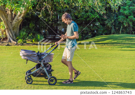 Father pushing a baby stroller on a grassy field while looking at his phone. Concept of modern parenting, multitasking, technology in daily life, and work-life balance 124863743