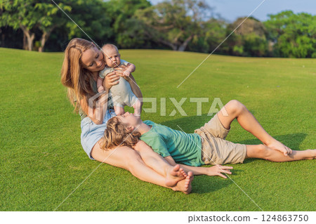 Mother, older son, and newborn baby on a meadow in the park. Family spending quality time together in nature. Parenthood, love, and family bond concept 124863750