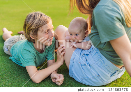 Mother, older son, and newborn baby on a meadow in the park. Family spending quality time together in nature. Parenthood, love, and family bond concept Mother, older son, and newborn baby on a meadow in the park. Family spending quality time together in nature. Parenthood, love, and family bond concept 124863778