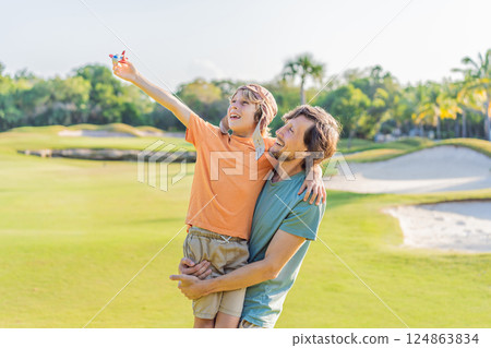 Father and son in the park, the boy wearing a pilot hat and holding a toy airplane, dreaming of adventures. Childhood, bonding, and imagination concept Father and son in the park, the boy wearing a pilot hat and holding a toy airplane, dreaming of adventures. Childhood, bonding, and imagination concept 124863834