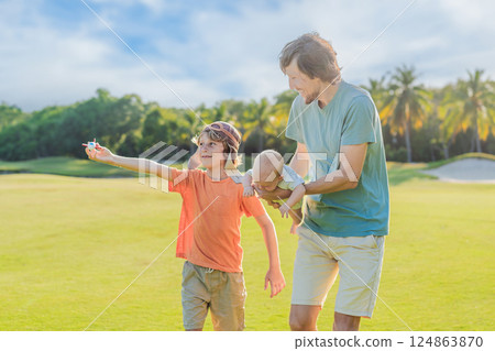Father with his two sons in the park, the older boy wearing a pilot hat and holding a toy airplane while the baby watches. Childhood, bonding, and family adventure concept Father with his two sons in the park, the older boy wearing a pilot hat and holding a toy airplane while the baby watches. Childhood, bonding, and family adventure concept 124863870