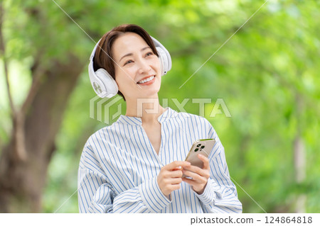 Woman listening to music with headphones, fresh greenery 124864818