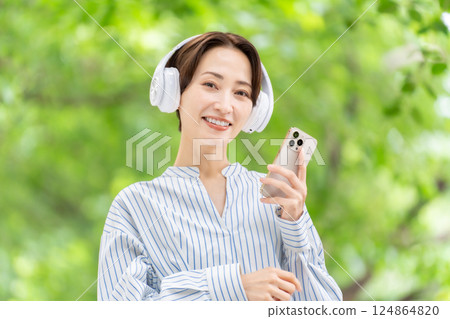 Woman listening to music with headphones, fresh greenery 124864820