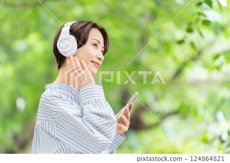 Woman listening to music with headphones, fresh greenery 124864821