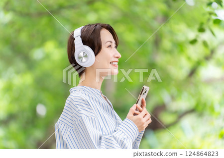 Woman listening to music with headphones, fresh greenery Woman listening to music with headphones, fresh greenery 124864823