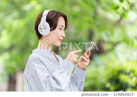 Woman listening to music with headphones, fresh greenery 124864825