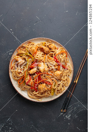Asian udon noodles with chicken and vegetables sprinkled with sesame seeds on dark background top view Asian udon noodles with chicken and vegetables sprinkled with sesame seeds on dark background top view 124865194