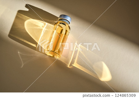 Injection vial with medicinal product in sunlight on beige background. 124865309
