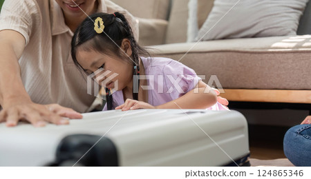 Playful Exploration and Child Development. A young girl focuses intently on her toy suitcase while her parents support her learning experience. Playful Exploration and Child Development. A young girl focuses intently on her toy suitcase while her parents support her learning experience. 124865346