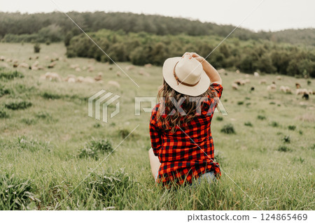 A woman wearing a straw hat sits in a field with a red and white plaid shirt A woman wearing a straw hat sits in a field with a red and white plaid shirt 124865469
