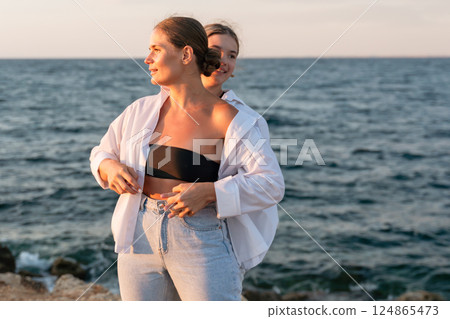 Couple Beach Sunset - Woman standing on a rocky beach with a man behind her at sunset looking out at the ocean. 124865473