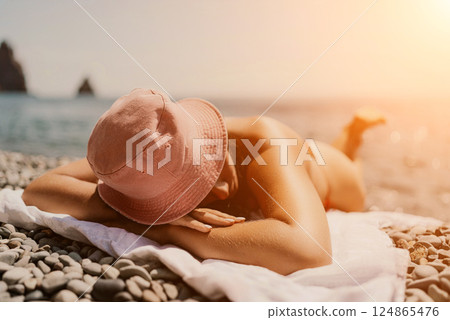 A woman sunbathes on the beach, lying on her stomach in a red swimsuit against the sea backdrop. 124865476