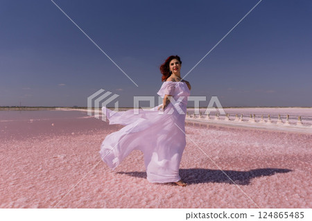 Woman Pink Salt Lake Dress - A woman in a white dress walks on a pink salt lake on a sunny day. Woman Pink Salt Lake Dress - A woman in a white dress walks on a pink salt lake on a sunny day. 124865485