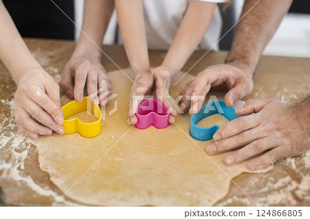 Family preparing cookies with hands using heart-shaped molds on rolled dough, showcasing teamwork. 124866805