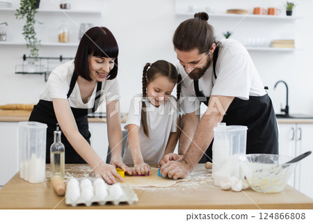 Caucasian family, young parents with child, baking cookies and enjoying quality time together. Image shows kitchen activities highlighting teamwork, happiness, and domestic life. 124866808