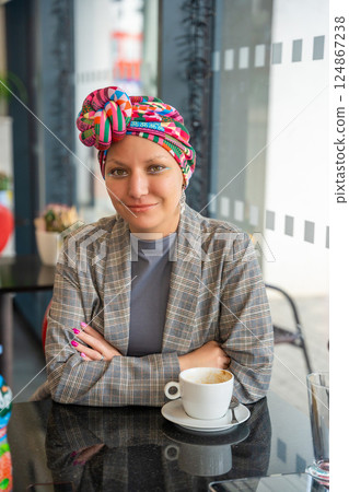 Stylish young woman in a turban sitting in a cafe, drinking coffee and enjoying the moment. The concept highlights that cancer patients can express their identity through fashion and live fully 124867238
