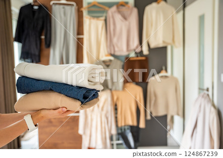 Stack of clothing in woman hands prepared for resale, donation, or recycling. Sustainable fashion choices support second-hand use, reduce waste, and promote conscious consumption 124867239