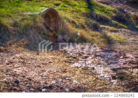 A concrete drainage pipe releases water into a stream, framed by grassy banks and sunlight. A concrete drainage pipe releases water into a stream, framed by grassy banks and sunlight. 124868241