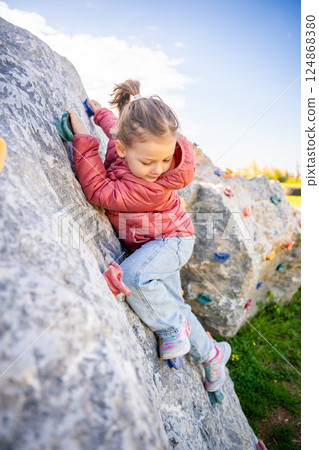 Little girl climbing an artificial climbing wall in a playground, developing strength and coordination 124868380