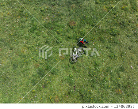 Aerial view of woman riding mountain bike on flowering grassland mountain 124868955