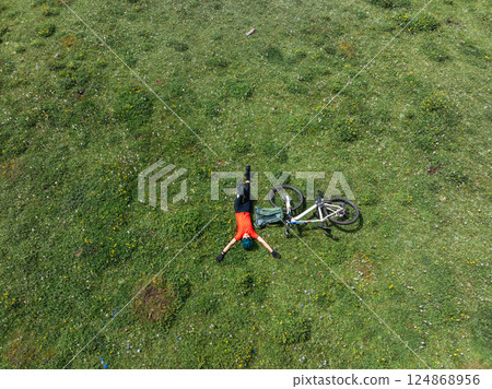 Aerial view of woman cyclist with mountain bike on flowering grassland mountain 124868956